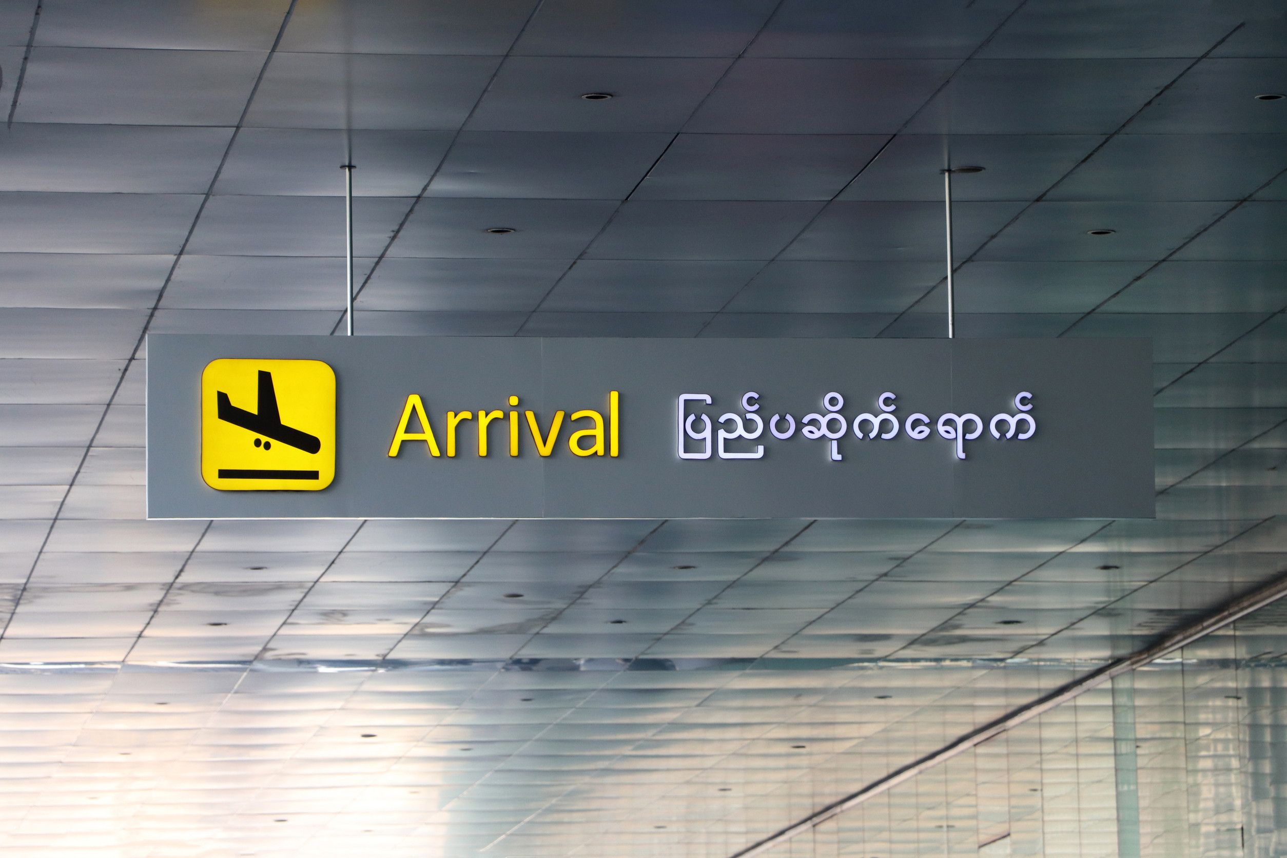 Arrival sign in English and Myanmar language with symbol of the plane landing in black on yellow