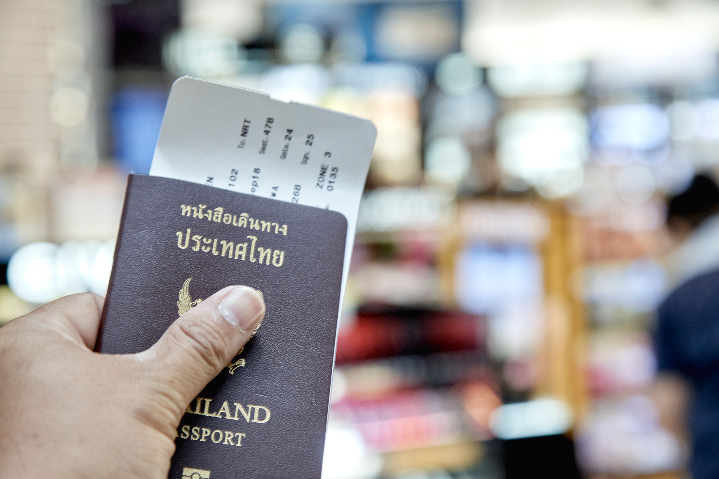 Man Left Hand Holding Thailand Passport With Airport Flight Schedule Blurred Travel Concept