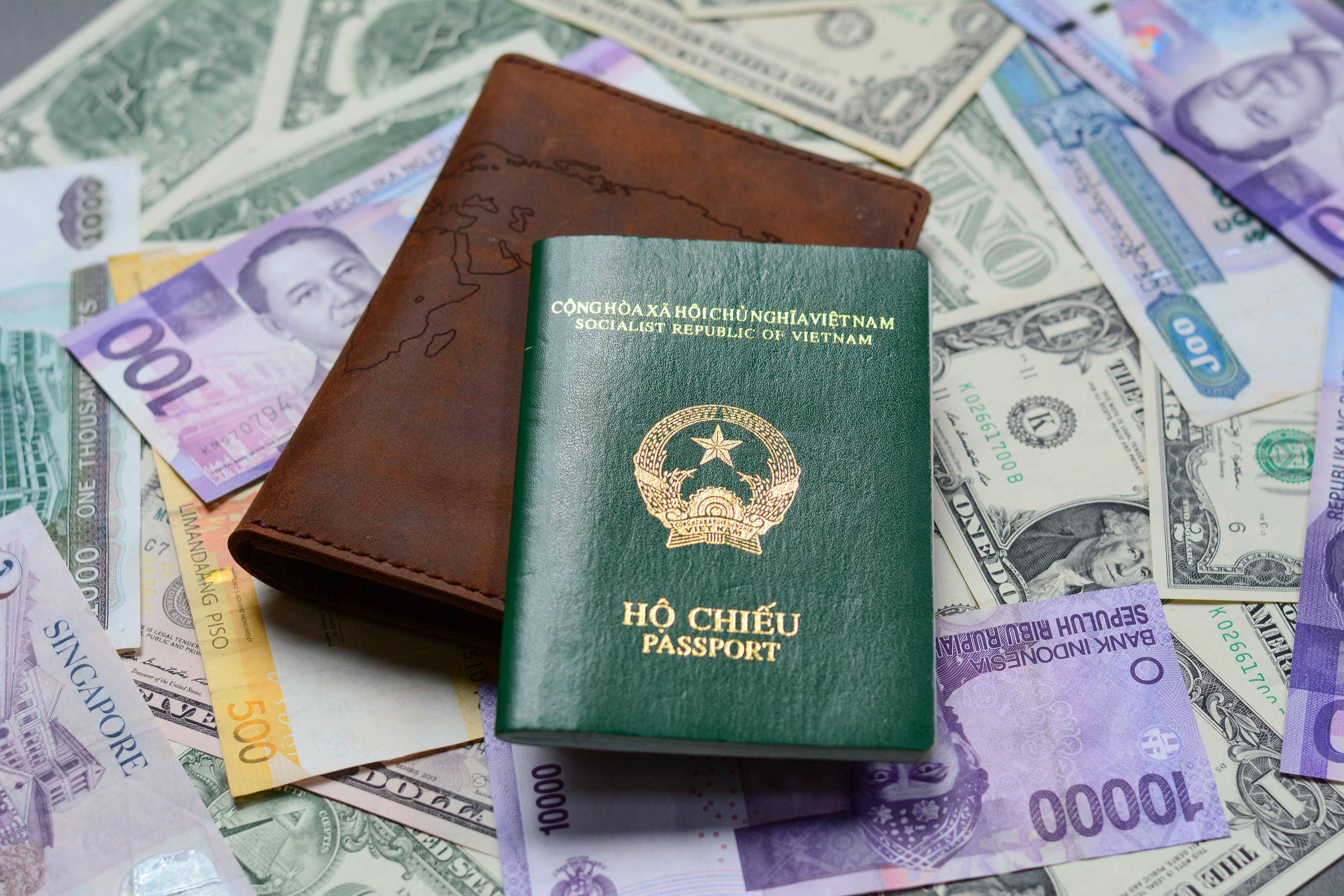Many Banknotes Of Different Countries With A Passport Scattered On The Table Closed