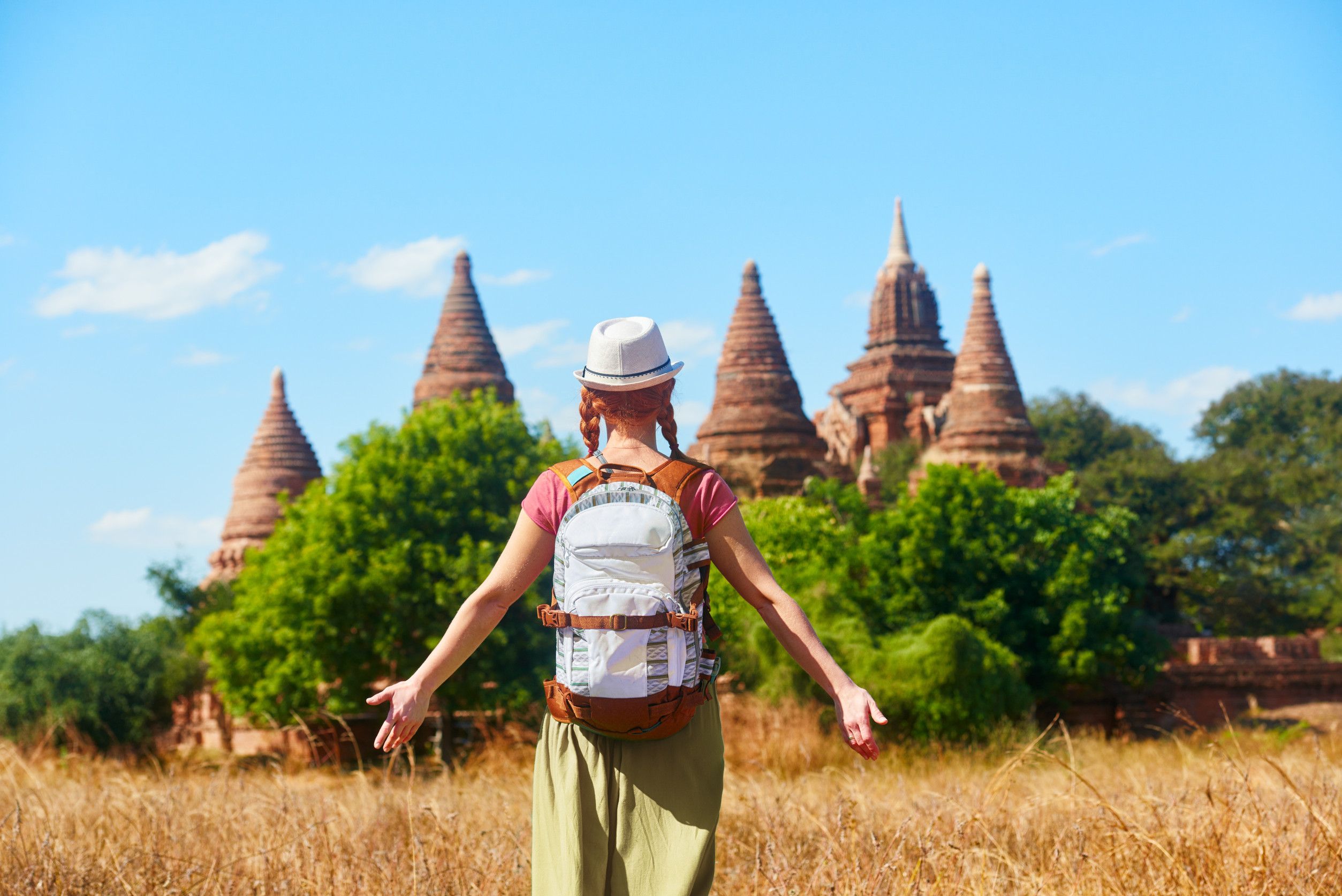 Rear view of woman traveler with a backpack walking through the field to the ancient Buddhist stupas