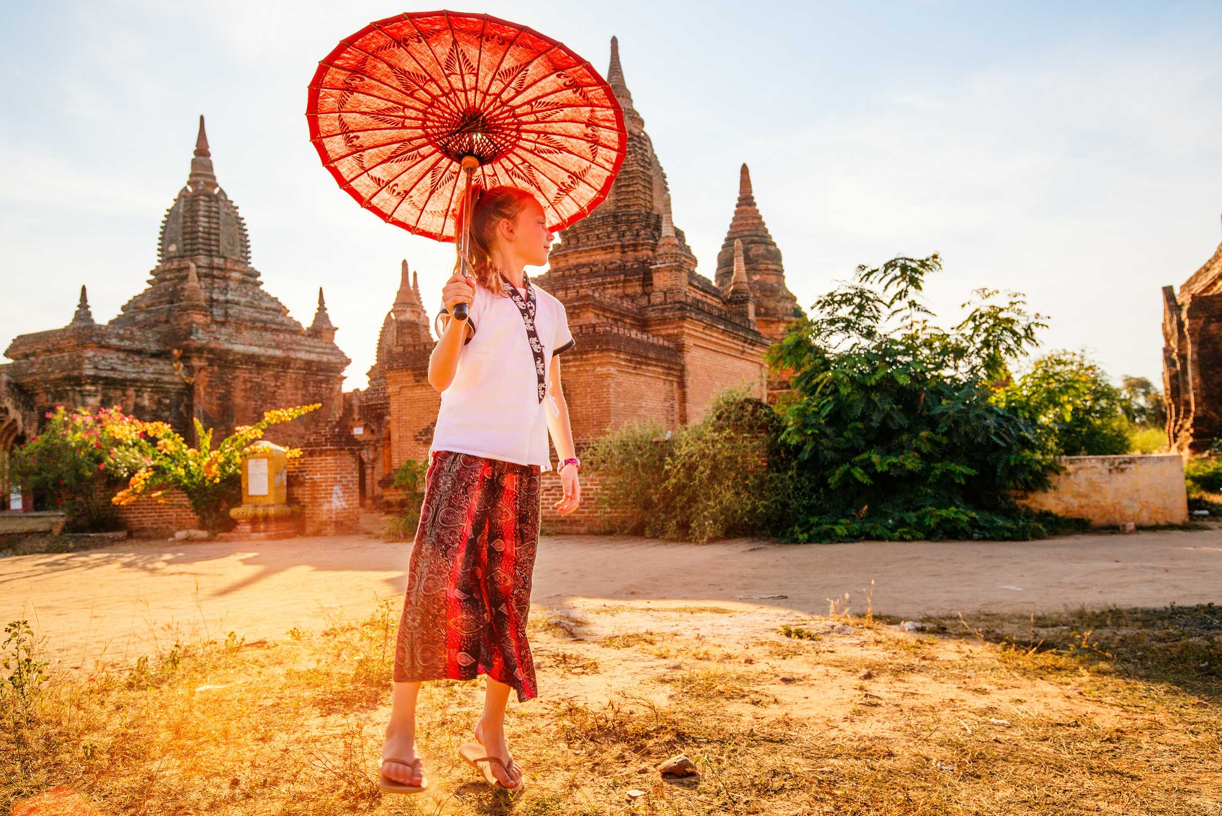 Young girl with traditional Burmese parasol visiting ancient temples in Bagan Myanmar at sunset